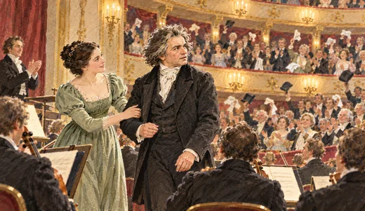 Illustration of a singer guiding a composer to turn toward a cheering audience beside an orchestra.